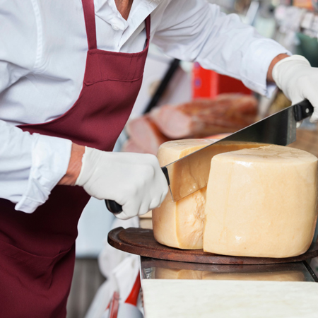 Mitarbeiter schneidet Stücke aus einem Großen Laib Käse
