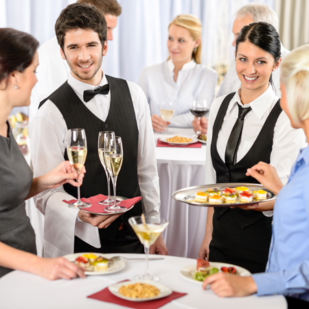 Eine Kellnerin und ein Kellner die Sekt und Häppchen servieren